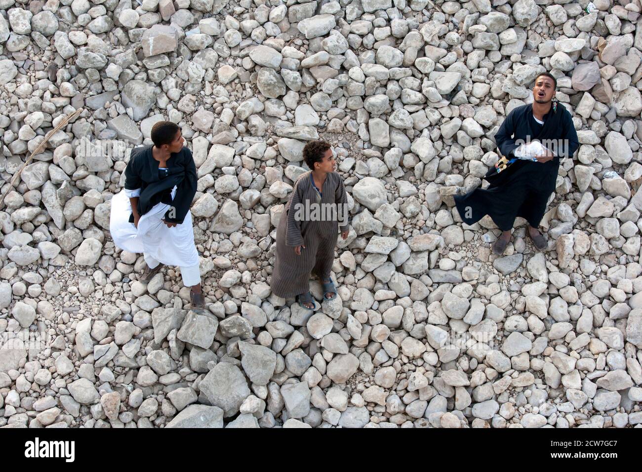 I ragazzi egiziani si ergono sulla riva rocciosa del fiume Nilo, accanto alla chiusa di Esna in Egitto, mentre passa accanto a un hotel galleggiante. Foto Stock