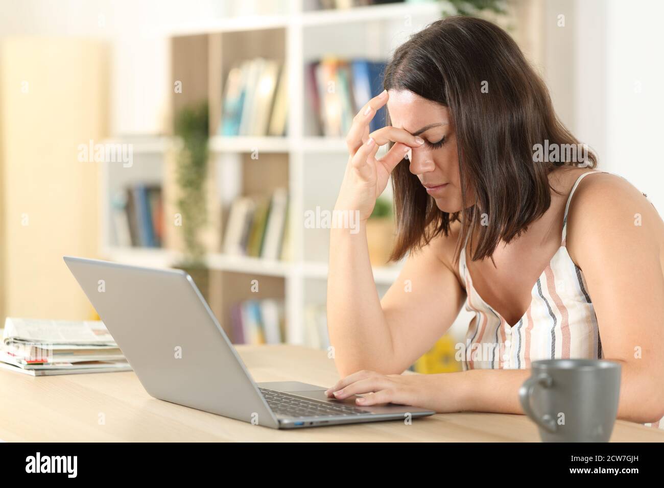 Donna stanca che soffre di vista con un computer portatile su una scrivania a casa Foto Stock