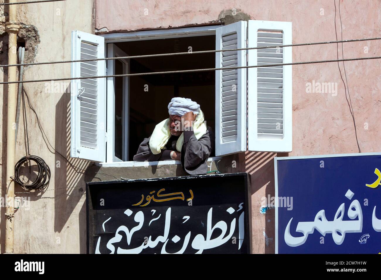 Un uomo egiziano fa un'indagine sulle strade trafficate di Edfu in Egitto da una finestra in un edificio di appartamenti. Foto Stock