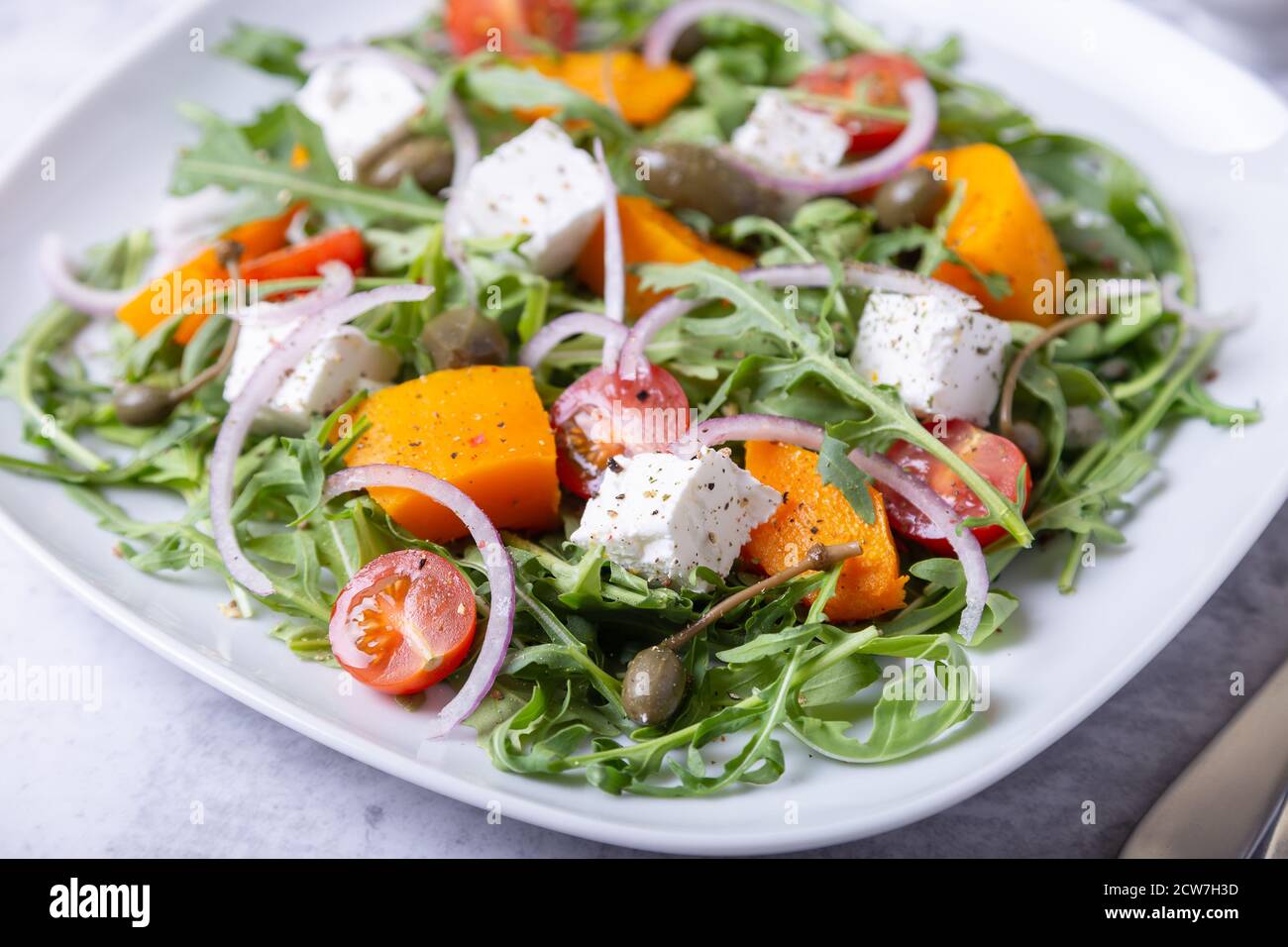 Insalata calda con zucca, formaggio feta, pomodori, capperi, rucola e cipolla rossa. Primo piano. Foto Stock