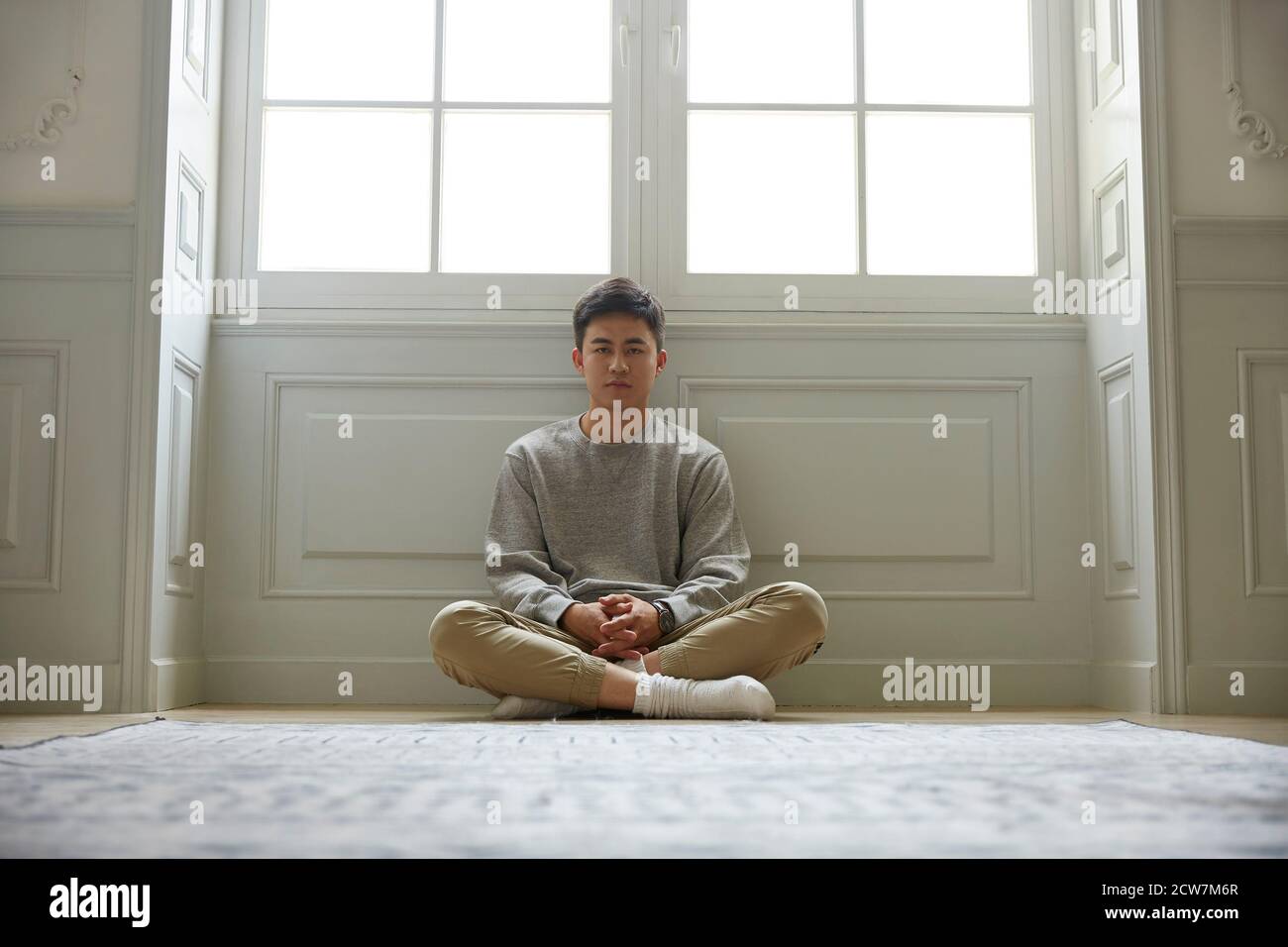 giovane asiatico seduto sul pavimento a casa gambe incrociate guardando la fotocamera Foto Stock
