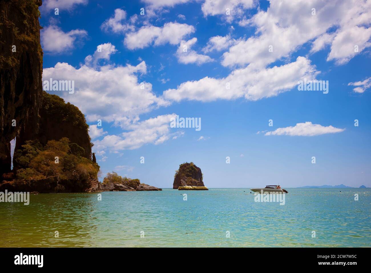 La roccia in mare è dipinta con oro. Il motoscafo galleggia nelle vicinanze. Cielo blu, un sacco di nuvole. Spiaggia di Cave. Pranang, provincia di Krabi Foto Stock