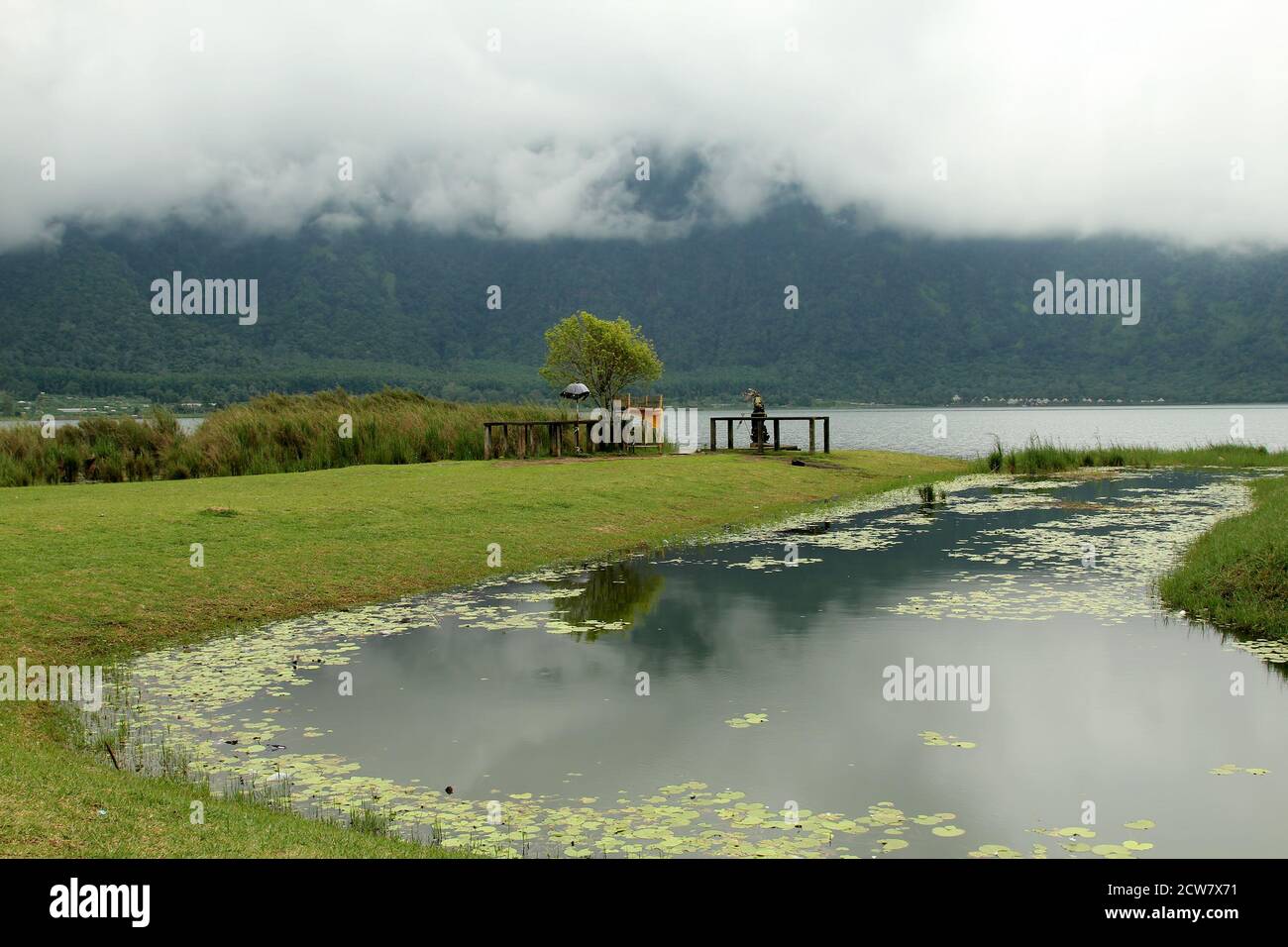 Luogo di preghiera e di potere. Lago Bratan in nebbia. Offerte rituali balinesi tradizionali in cesti di paglia per spiriti indù e dèi con fiori e bastoncini aromatici Foto Stock