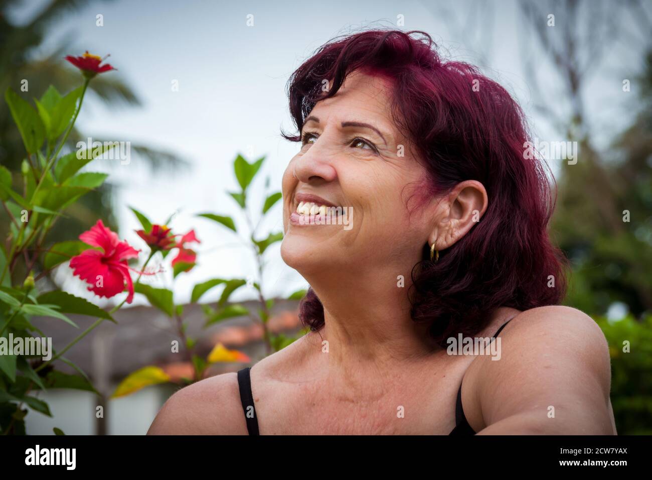 Ritratto di una bella donna latina di mezza età all'aperto dentro il giardino con i suoi capelli appena tinti in un piatto colore Foto Stock