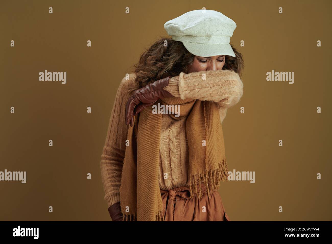 Ciao autunno. Donna elegante in pullover con guanti in pelle starnutire a gomito su sfondo marrone. Foto Stock