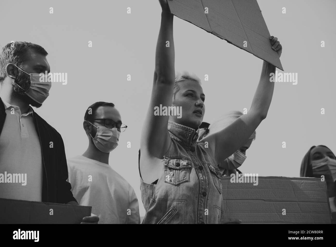 Bianco e nero. Gruppo di attivisti che danno slogan in un rally. Uomini e donne caucasici che marciano insieme in una protesta in città. Guarda arrabbiato, fiducioso, fiducioso. Banner vuoti per il tuo disegno o annuncio. Foto Stock