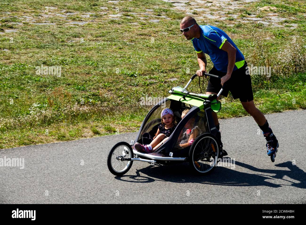 Uomo pattinaggio a rotelle e passeggino con due bambini in un passeggino a tre ruote, corsa Foto Stock