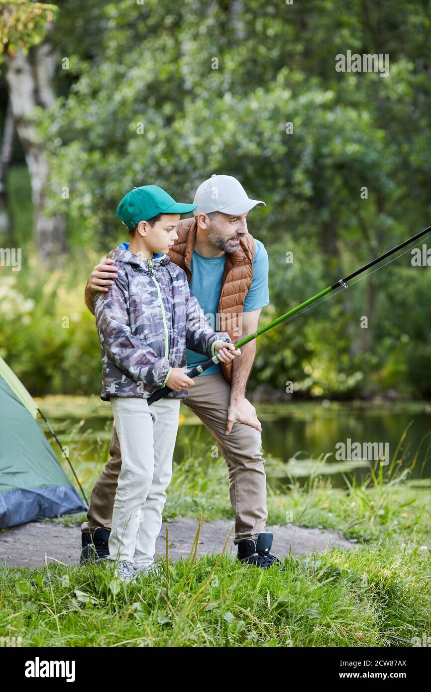 Verticale vista laterale ritratto del padre amorevole insegnare la pesca del figlio mentre ti godi il campeggio insieme Foto Stock
