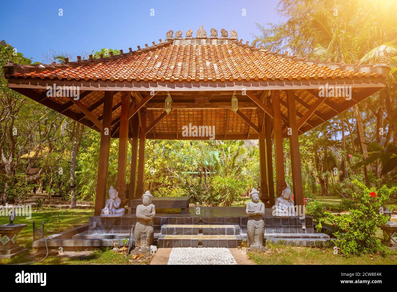Antico padiglione gazebo con tetto in stile asiatico pagoda. In un giardino  tropicale estivo soleggiato. Un sentiero in pietra lungo il quale si  trovano le statue conduce all'IT.Inside l'area di riposo e