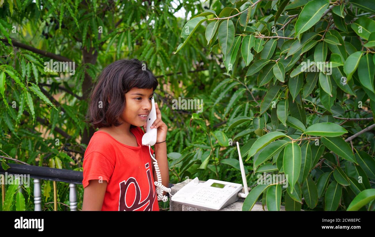 Piccola ragazza indiana con il vecchio telefono wireless e foglie verdi di sfondo. Foto Stock