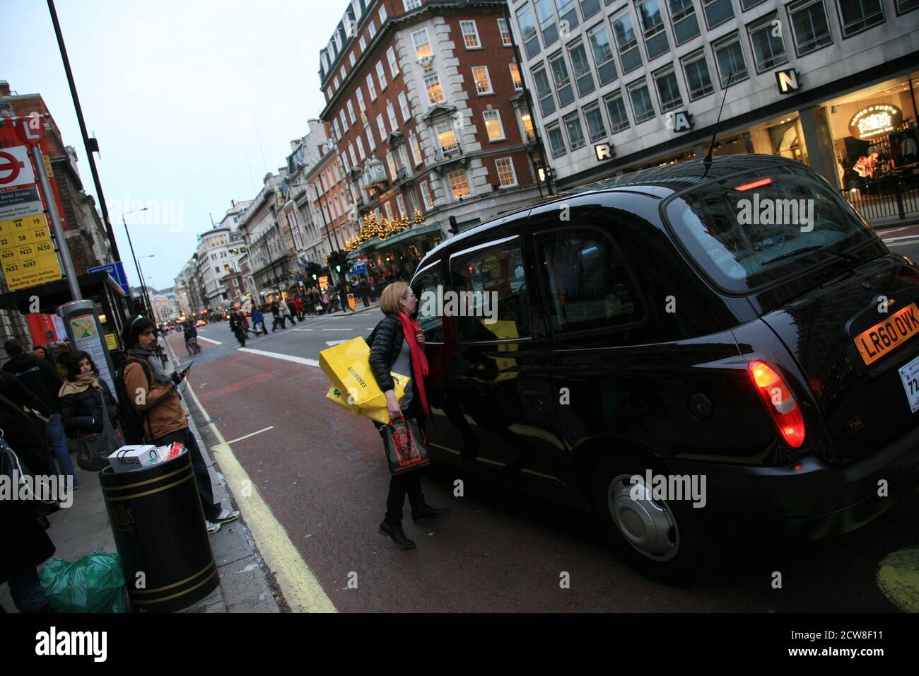 Londra, Regno Unito - 13 novembre 2010: Taxi nella strada di Londra. Passeggero donna con borse per la spesa che chiede all'autista prima di salire a bordo. Le cabine nere sono il Foto Stock