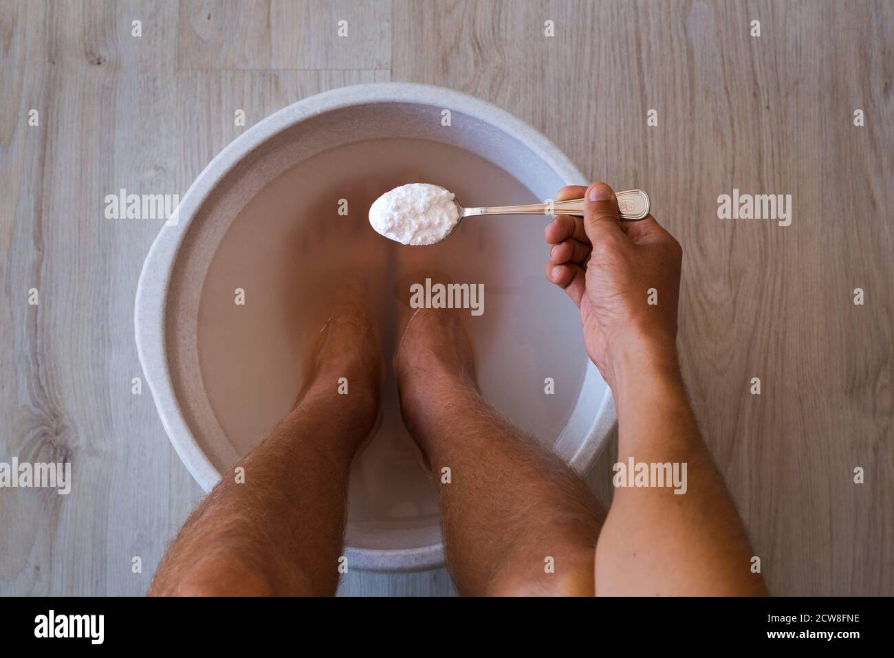 Uomo mise un cucchiaio di bicarbonato di sodio in bagno con acqua calda per  i suoi piedi. Bagnomaria fatta in casa per la pelle asciutta dei piedi Foto  stock - Alamy
