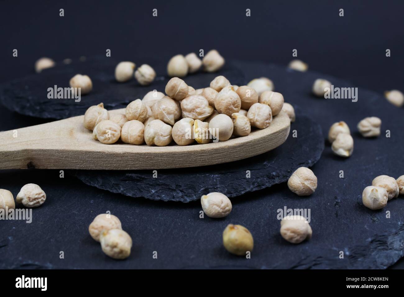 Macro closeup di cucchiaio di legno isolato con ceci crudi non cotti (chana dhal) su sfondo di pietra ardesia nera Foto Stock