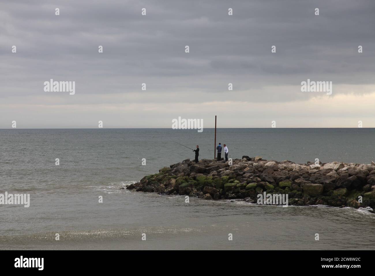Pescatori pesca marittima alla fine di un groyne di pietra, Dorset, Inghilterra Foto Stock