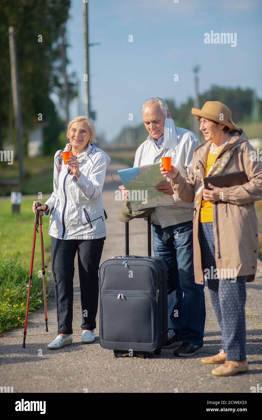 Gruppo di anziani positivi che guardano alla mappa del viaggio durante la pandemia.COVID-19 viaggio nella nuova normalità. Foto Stock