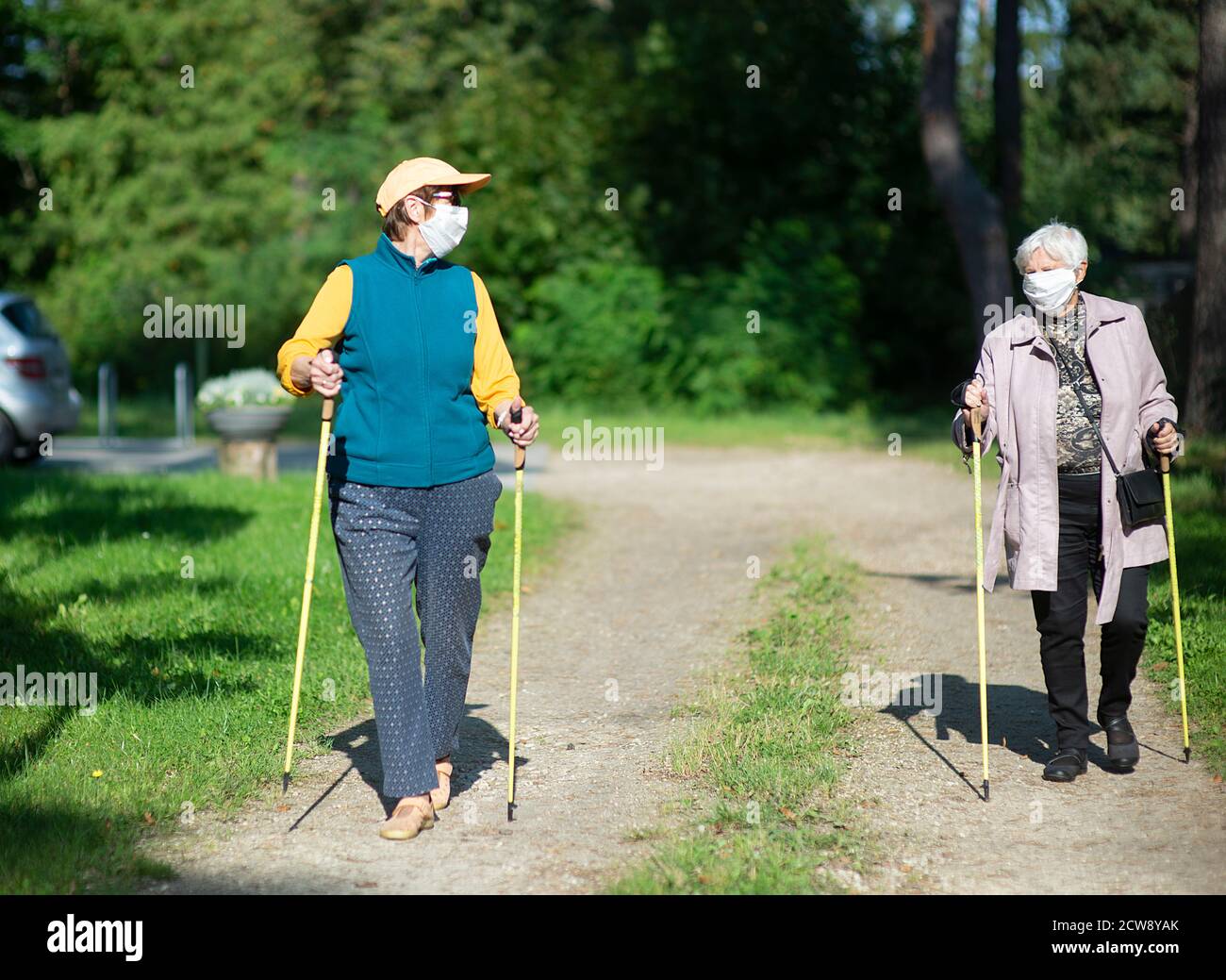 Due donne anziane che indossano maschere mediche che camminano con nordic walking poli durante la pandemia di covid-19 Foto Stock