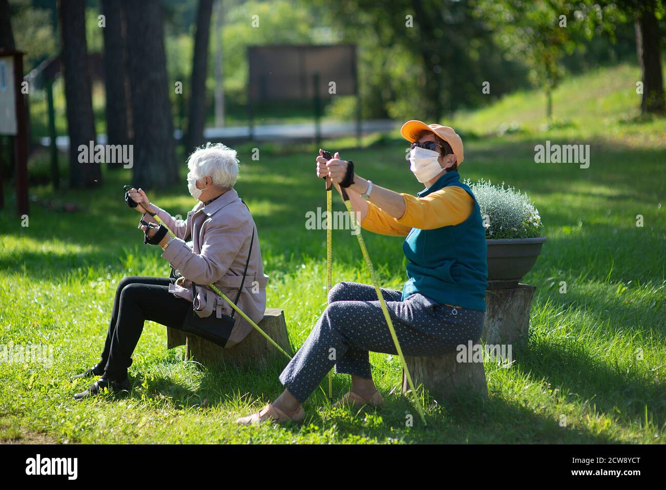 Due donne anziane senior con maschere viso riposano dopo un Nordic walking durante la pandemia COVID-19 Foto Stock