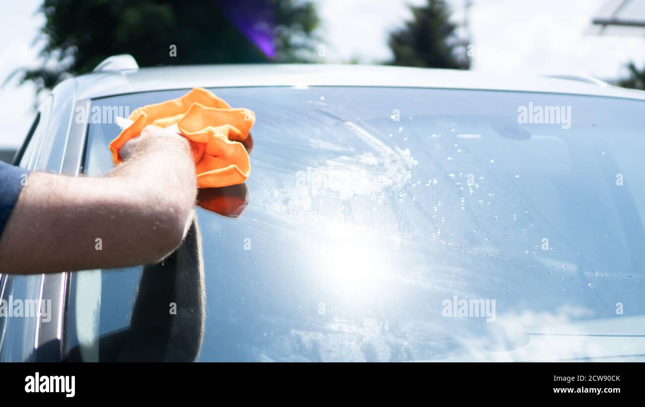 Pulire a mano il parabrezza di un'auto in una giornata di sole. Asciugare  con un panno arancione. Straccio rimuove le macchie d'acqua sulla finestra  Foto stock - Alamy