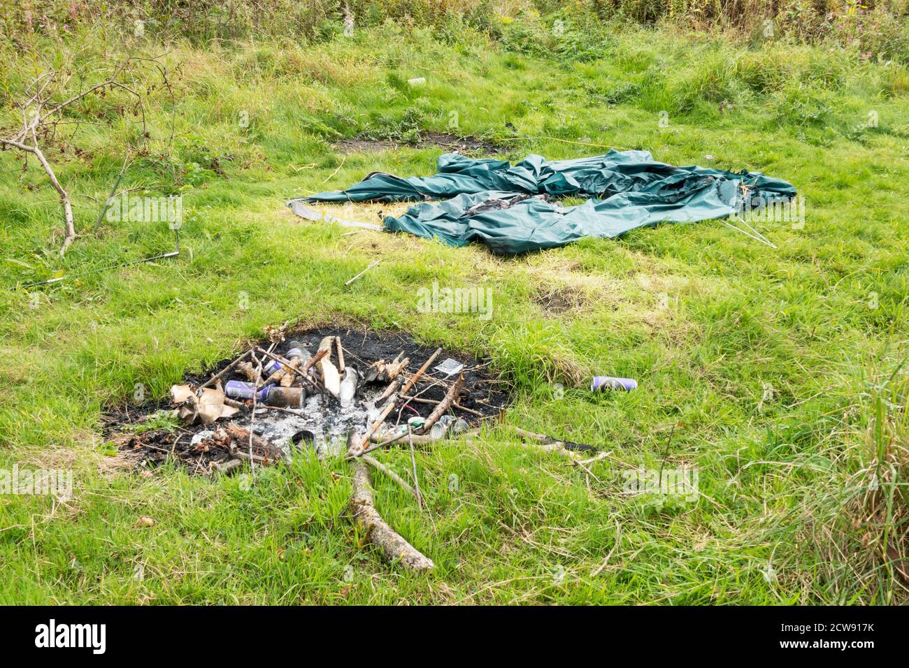 Tenda abbandonata e fuoco di accampamento con lattine e bottiglie di bevande scartate, campeggio illegale, Inghilterra nord-orientale, Regno Unito Foto Stock