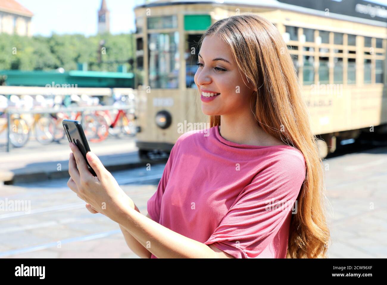 Bella giovane donna che tiene in mano lo smartphone in strada con il  vecchio tram che passa sullo sfondo a Milano, Italia Foto stock - Alamy