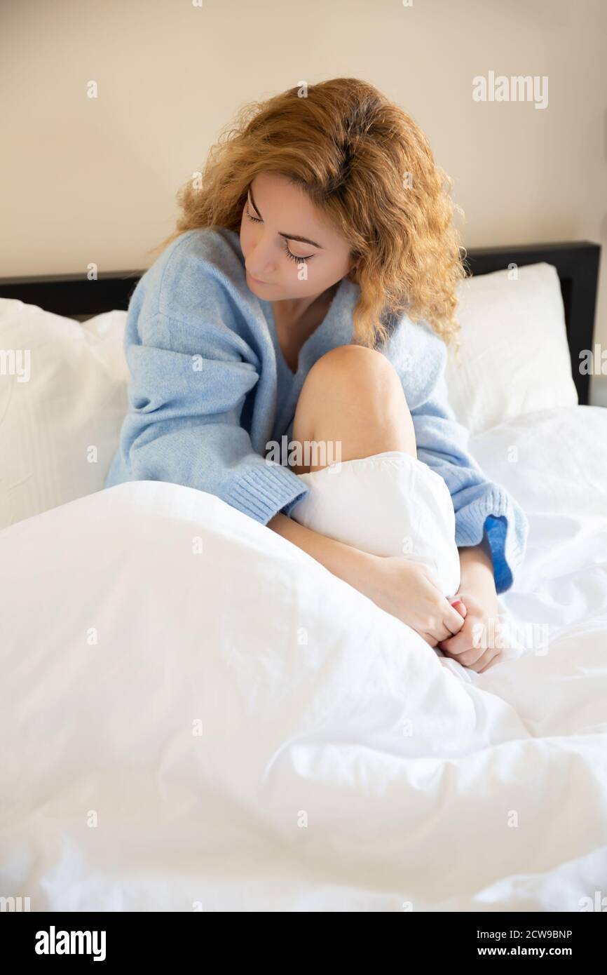 Donna in pullover blu seduta nel letto. Foto Stock