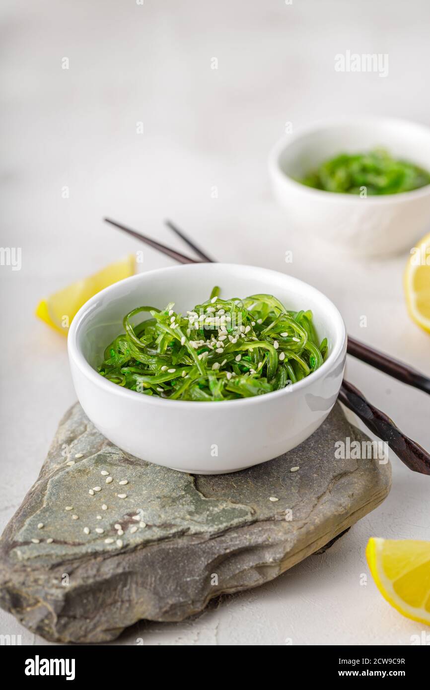 Foto ritagliata di insalata verde di alghe di wakame con bastoncino e. limone al ristorante Foto Stock