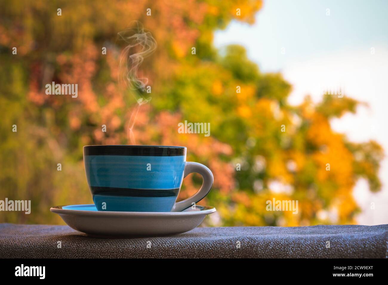 Tazza blu con bevanda calda su sfondo giallo autunno fogliame. Concetto di caduta. Primo piano Foto Stock