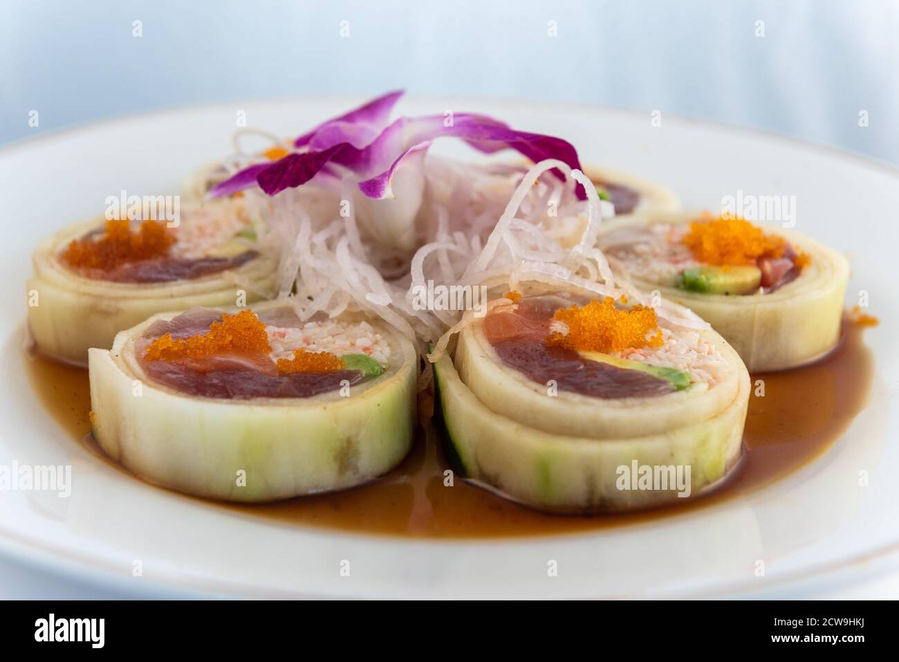 Pesce crudo assortito disposto in rotolo di suhshi rivestito con cetriolo delicatamente presentato su un piatto da mangiare. Foto Stock