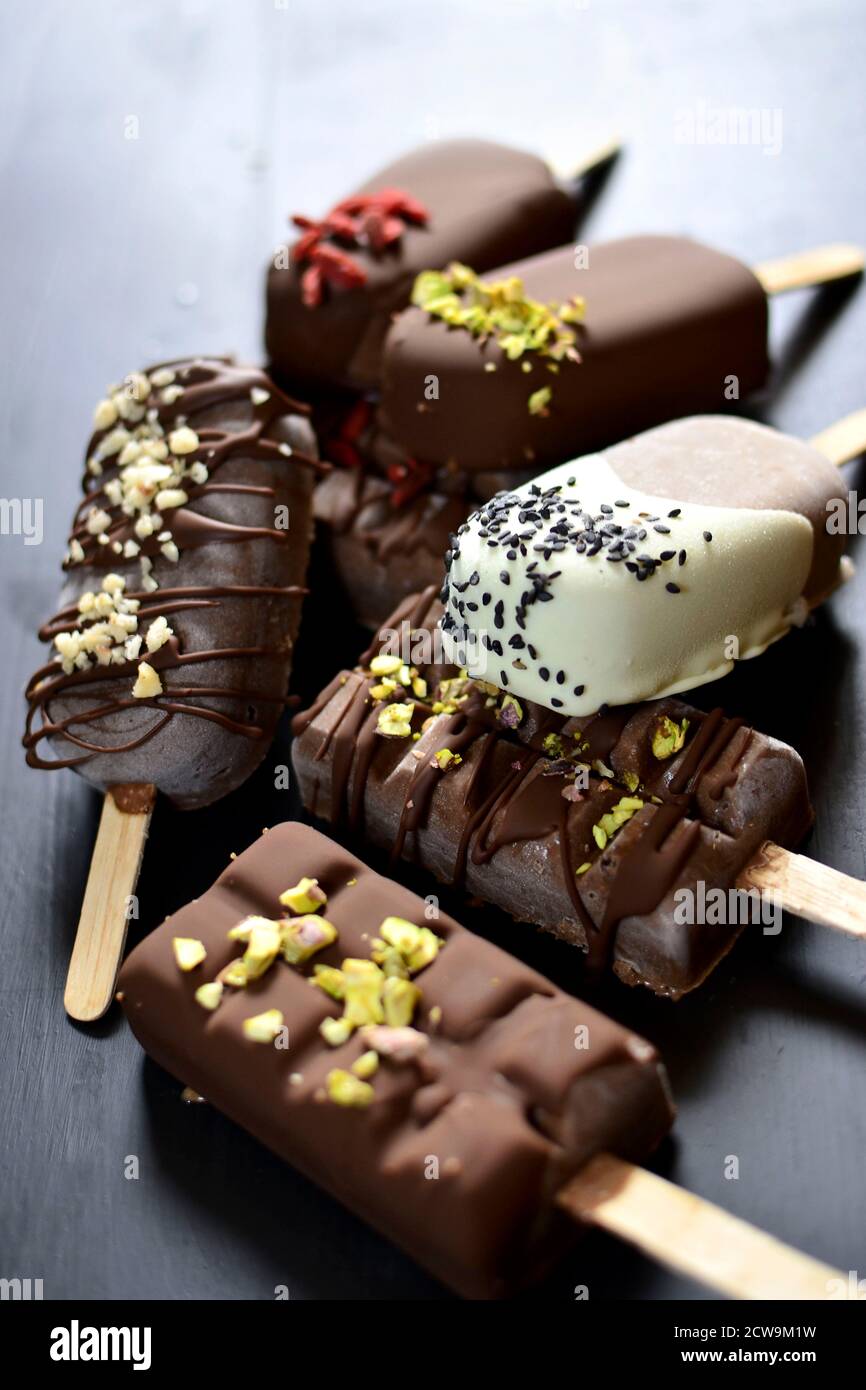 Uno scatto ravvicinato che mostra le mani di uno chef che decora una gelateria gourmet al cioccolato. Il dessert è immerso nel cioccolato fondente e cosparso di Foto Stock