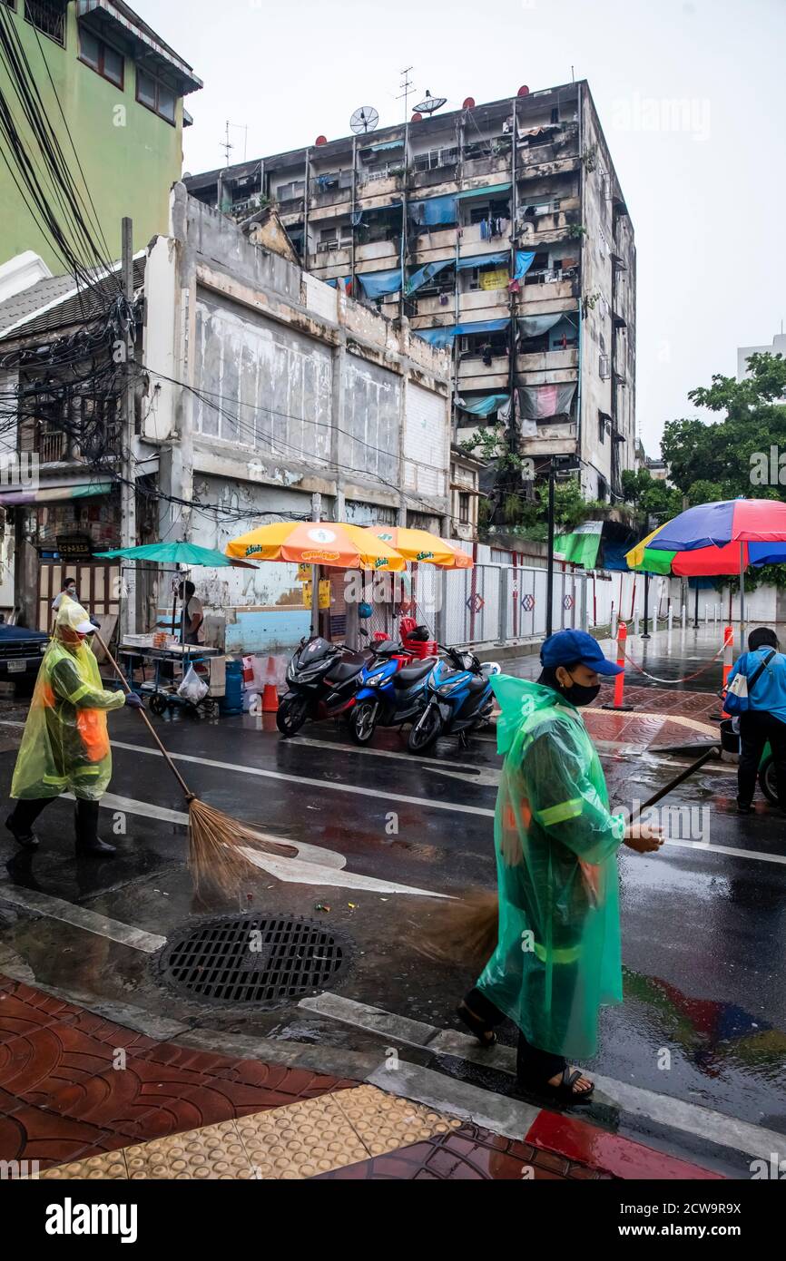 Due spazzatrici di strada usano la sua scopa per spingere l'acqua piovana in una tempesta di drenaggio nella Chinatown di Bangkok. Foto Stock