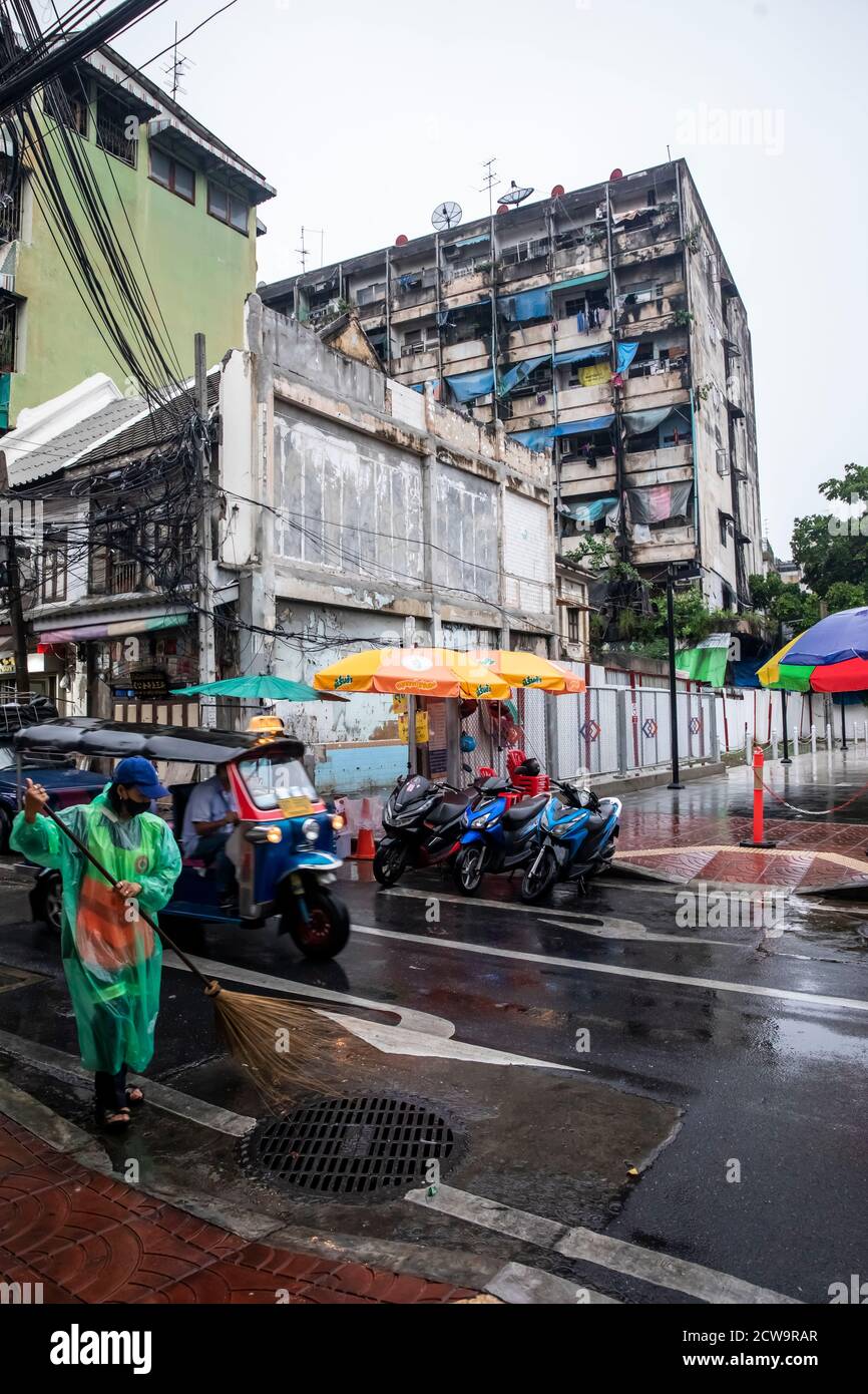 Una spazzatrice stradale usa la sua scopa per spingere l'acqua piovana in una tempesta di drenaggio nella Chinatown di Bangkok. Foto Stock