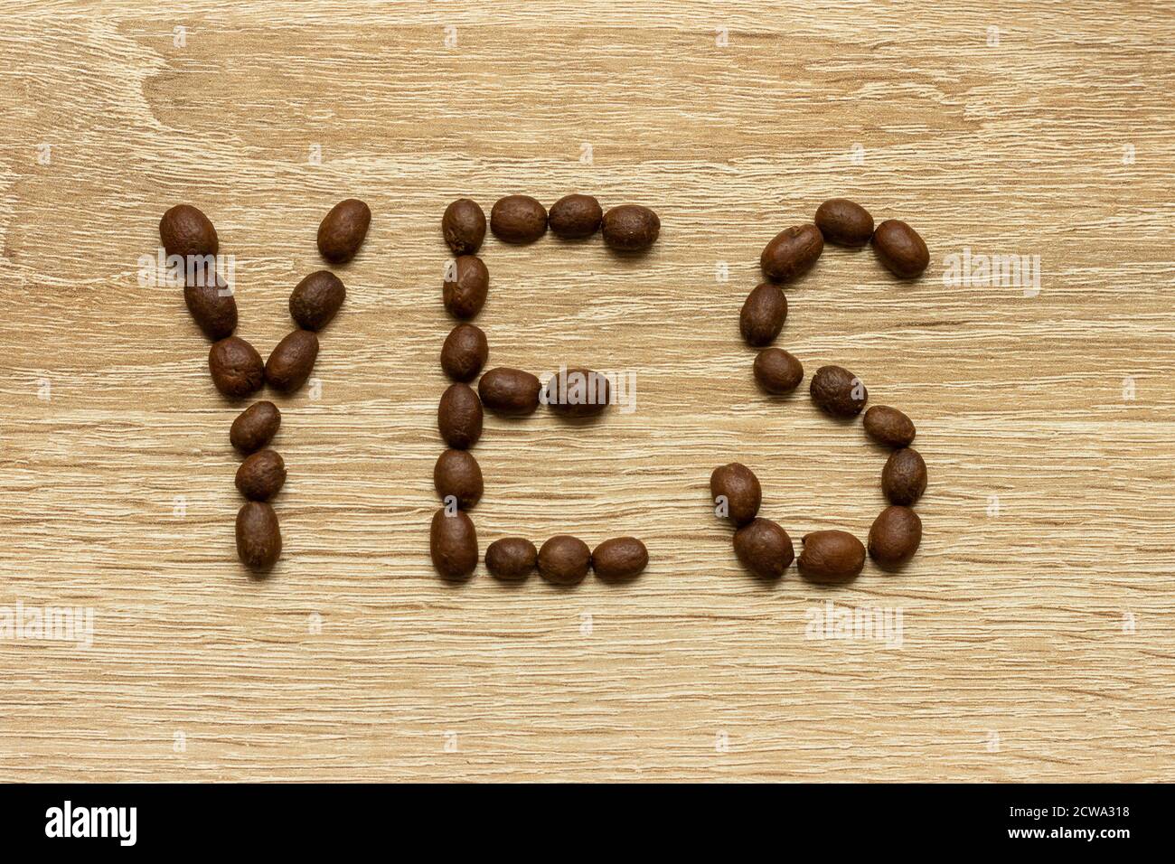 La parola "Sì" è riportata con i chicchi di caffè arabica tostati su un tavolo di legno. Foto Stock