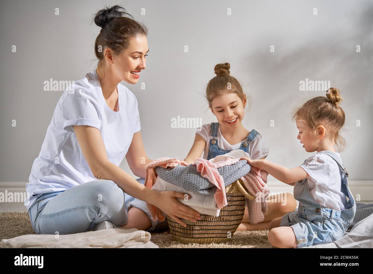 Bella giovane donna e bambini ragazze aiutanti poco stanno avendo divertimento e sorridendo mentre facendo lavanderia a casa. Foto Stock