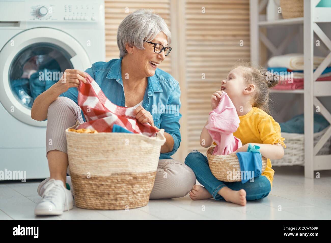 Felice nonna e bambino ragazza piccolo helper stanno avendo divertimento e sorridendo mentre facendo lavanderia a casa. Foto Stock