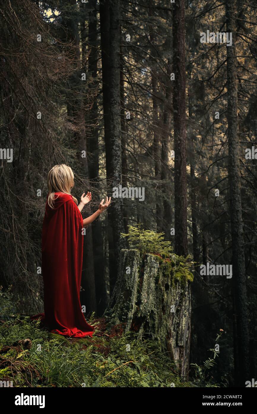 Donna con mantello rosso in preghiera nella foresta Foto Stock