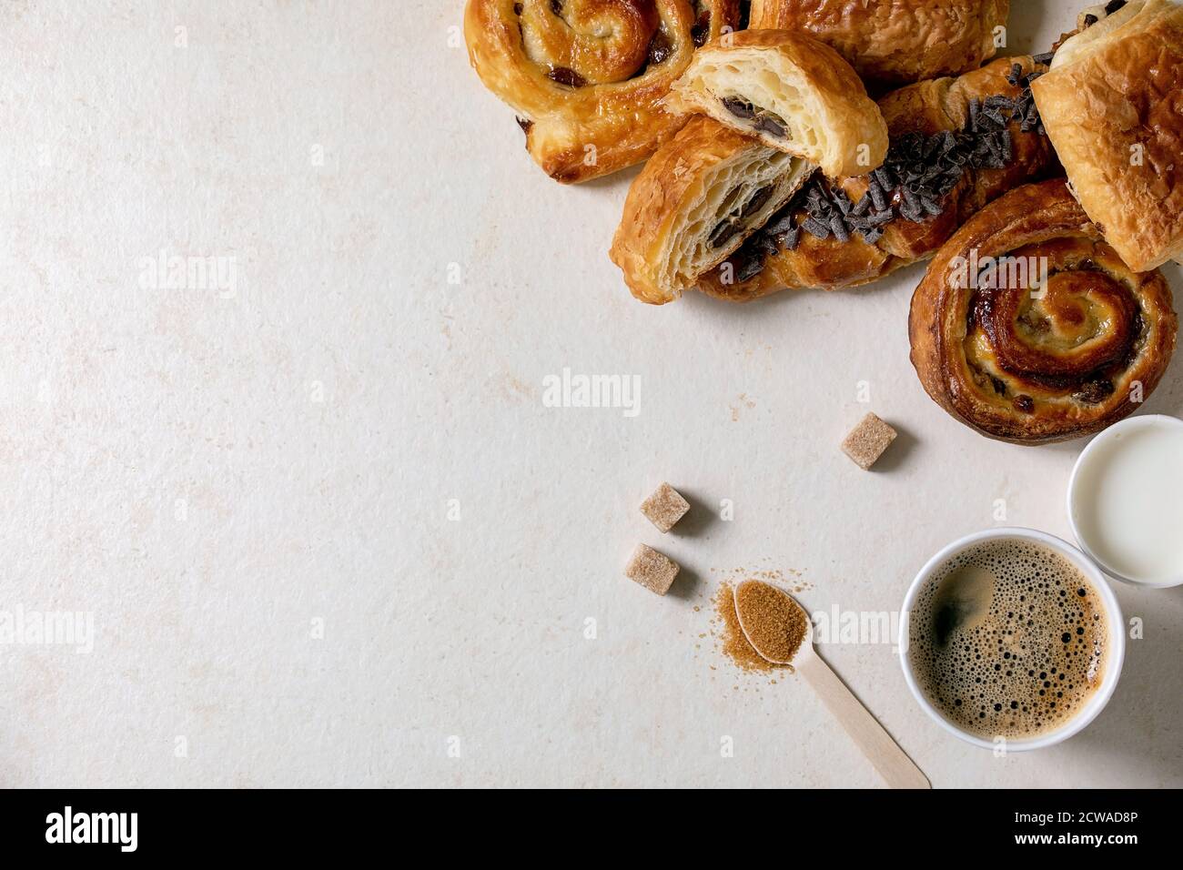 Varietà di panini tradizionali francesi con rasin e cioccolato, croissant con tazza di carta di caffè e latte, cucchiaio di legno riciclato di su di canna Foto Stock