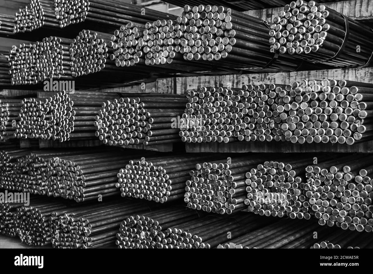 Stoccaggio e impilamento di file di barre rotonde in acciaio nel magazzino per l'edilizia industriale. Bianco e nero con messa a fuoco superficiale. Foto Stock