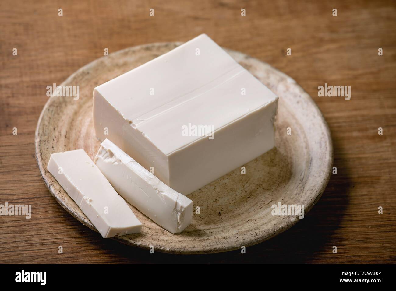 Tofu di seta giapponese formaggio di soia pezzo intero su piatto di ceramica con bastoni su tavolo di legno. Foto Stock