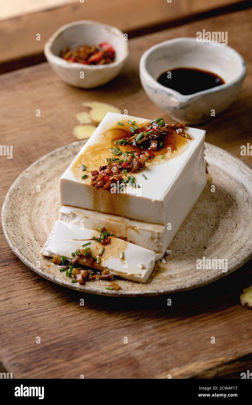 Tofu di seta giapponese formaggio di soia intero pezzo con peperoncino zenzero, erba cipollina e salsa di soia condimento su piastra di ceramica su tavolo di legno. Foto Stock