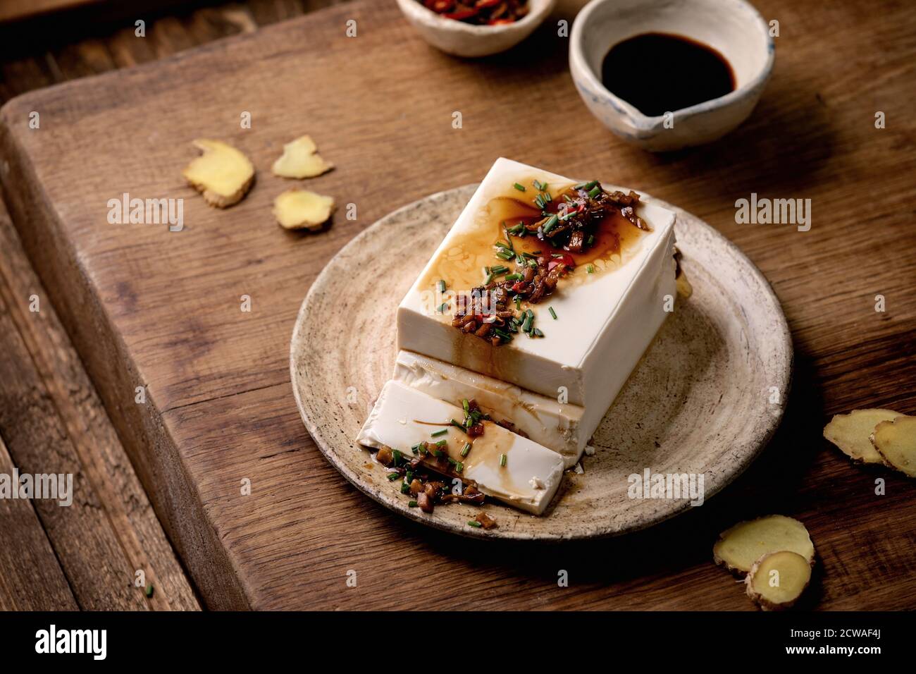 Tofu di seta giapponese formaggio di soia intero pezzo con peperoncino zenzero, erba cipollina e salsa di soia condimento su piastra di ceramica su tavolo di legno. Foto Stock