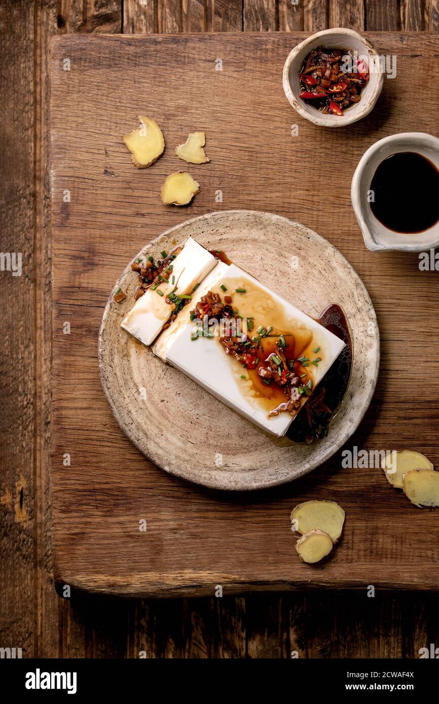 Tofu di seta formaggio giapponese di soia pezzo intero con zenzero di peperoncino, erba cipollina e salsa di soia, condimento su piastra di ceramica su tavolo di legno. Piatto, spazio Foto Stock
