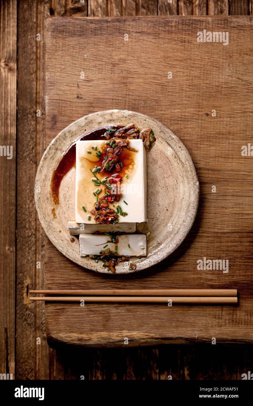 Tofu di seta giapponese formaggio di soia intero pezzo con peperoncino zenzero, erba cipollina e salsa di soia condimento su piastra di ceramica con bastoni su tavolo di legno. Piatto, Foto Stock