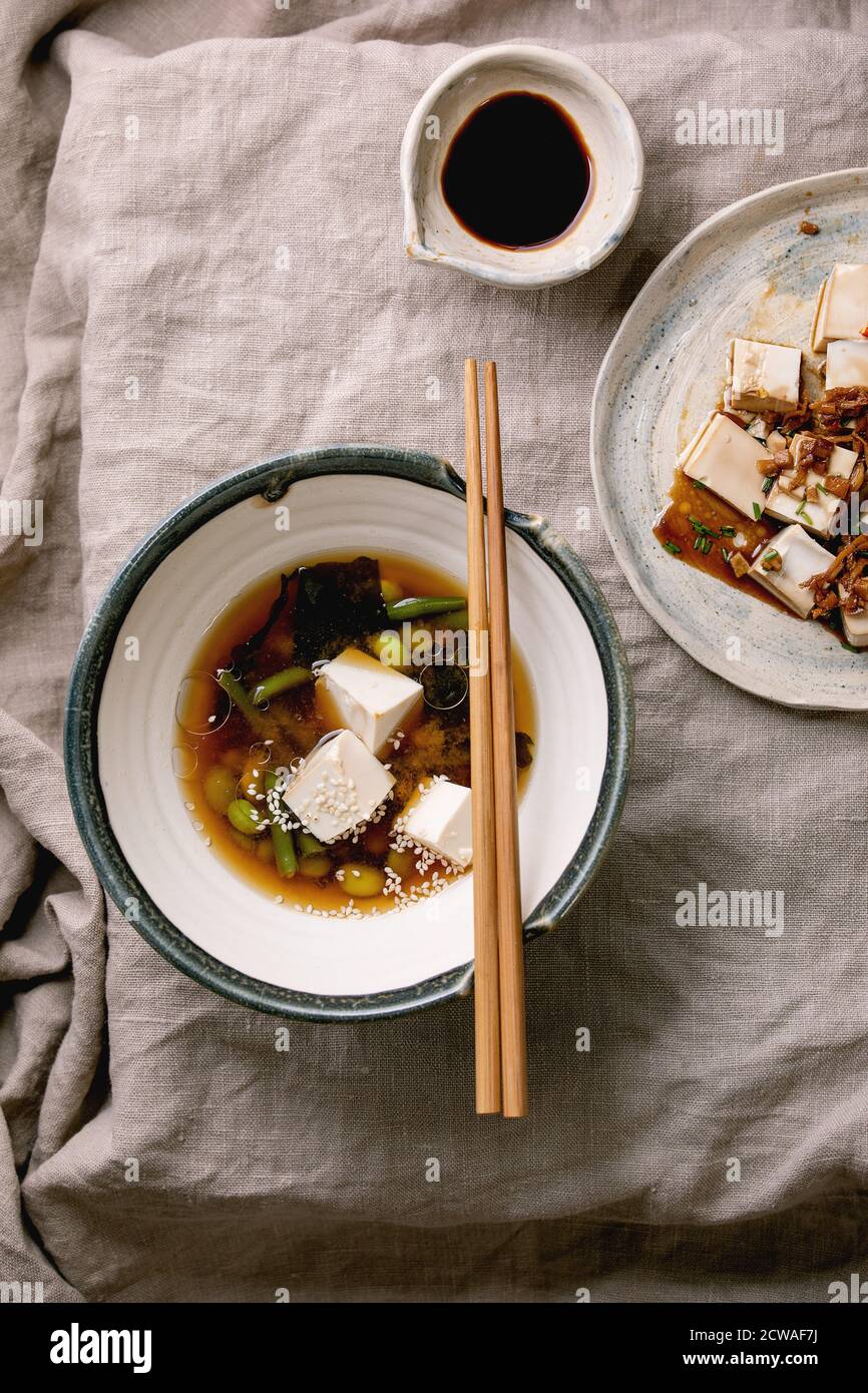 Zuppa giapponese di brodo miso con cubetti di tofu di seta, edamame di fagioli di soia, fagioli verdi in ciotola tradizionale con bastoncini di cotone su tovaglia di lino grigio. Din asiatico Foto Stock