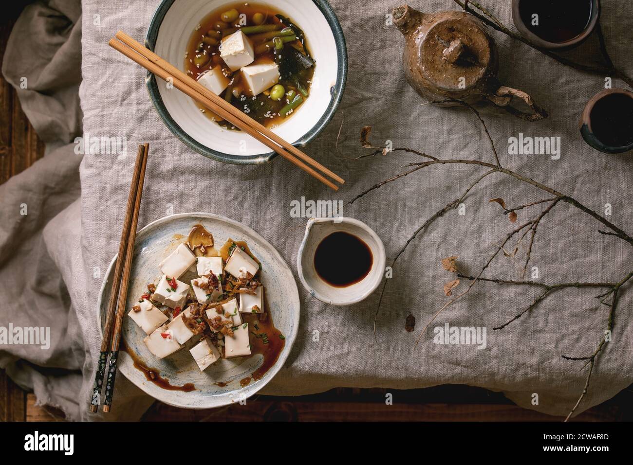 Zuppa giapponese di brodo miso con cubetti di tofu di seta, edamame di fagioli di soia, fagioli verdi in ciotola tradizionale con bastoncini, teiera in ceramica e tazze su lin grigio Foto Stock