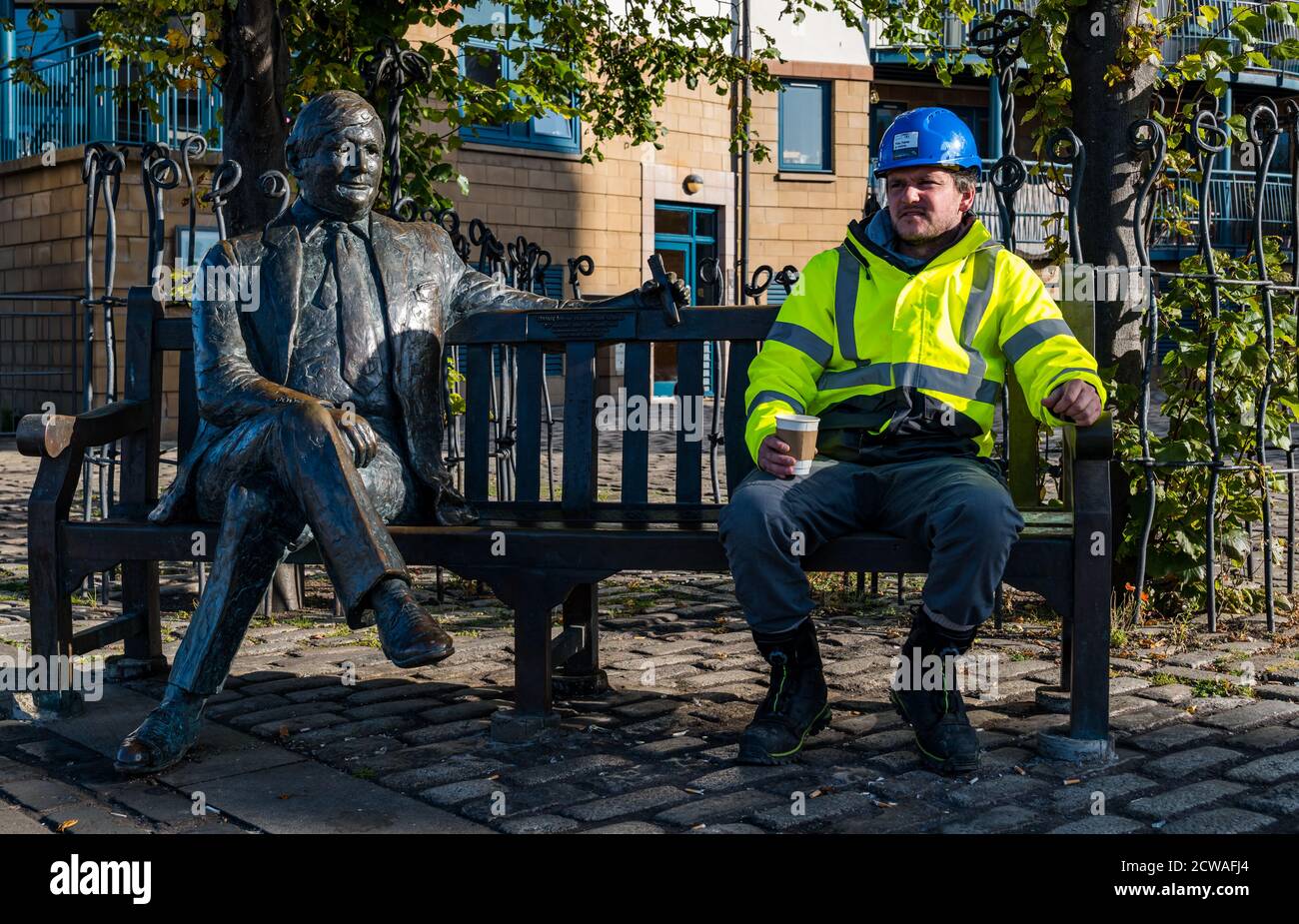 Leith, Edimburgo, Scozia, Regno Unito, 29 settembre 2020. Regno Unito Meteo: Sole su Leith. Un operaio prende una pausa mattutina seduto su una panchina bere caffè con la scultura a grandezza naturale di Sandy Robertson di Lucy Poett sulla riva Foto Stock