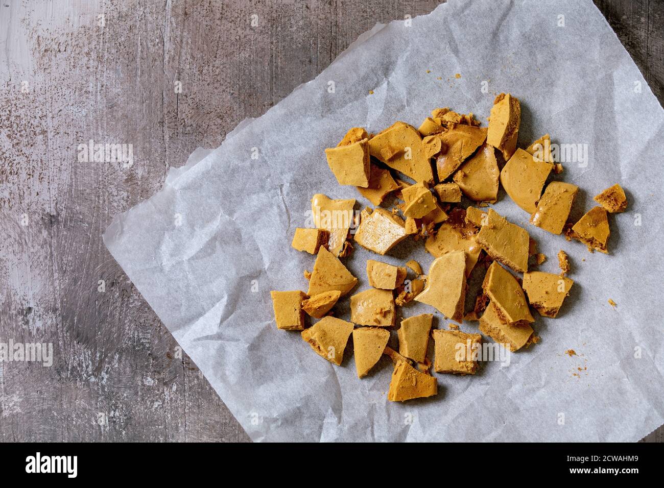 Pokey hokey a nido d'ape o tofee di cenere o caramelle di zucchero coreane di dalgona su carta da forno su fondo grigio di cemento. Piatto, spazio Foto Stock