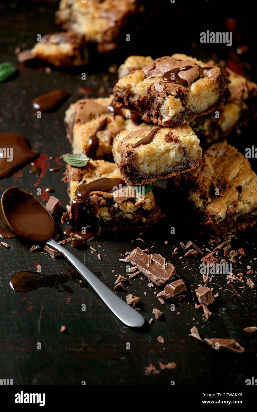 Trend Baking Brookies cioccolato brownie e biscotti torta fatta in casa tagliata da piazze in fila, salsa di cioccolato, menta su sfondo nero. Foto Stock