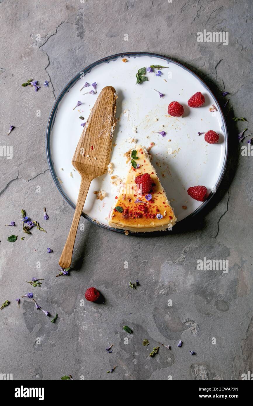 Ultimo pezzo di lampone cotto in casa cheesecake su piatto decorato da lamponi freschi e menta, con server torta di legno su sfondo grigio textute Foto Stock
