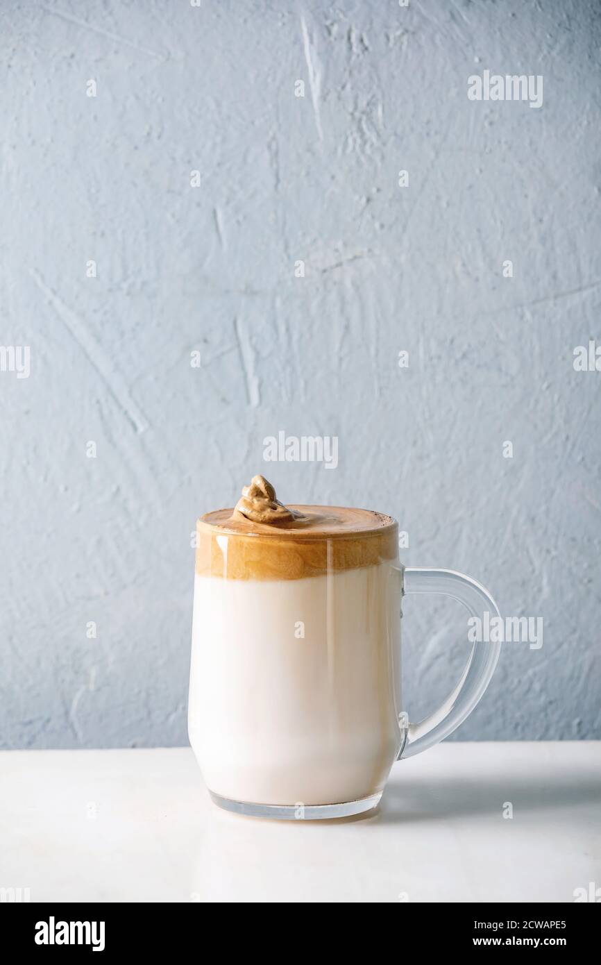 Dalgona Frothy caffè tendenza bevanda coreana latte latte latte con schiuma di caffè in tazza di vetro su tavolo di marmo bianco. Spazio di copia Foto Stock