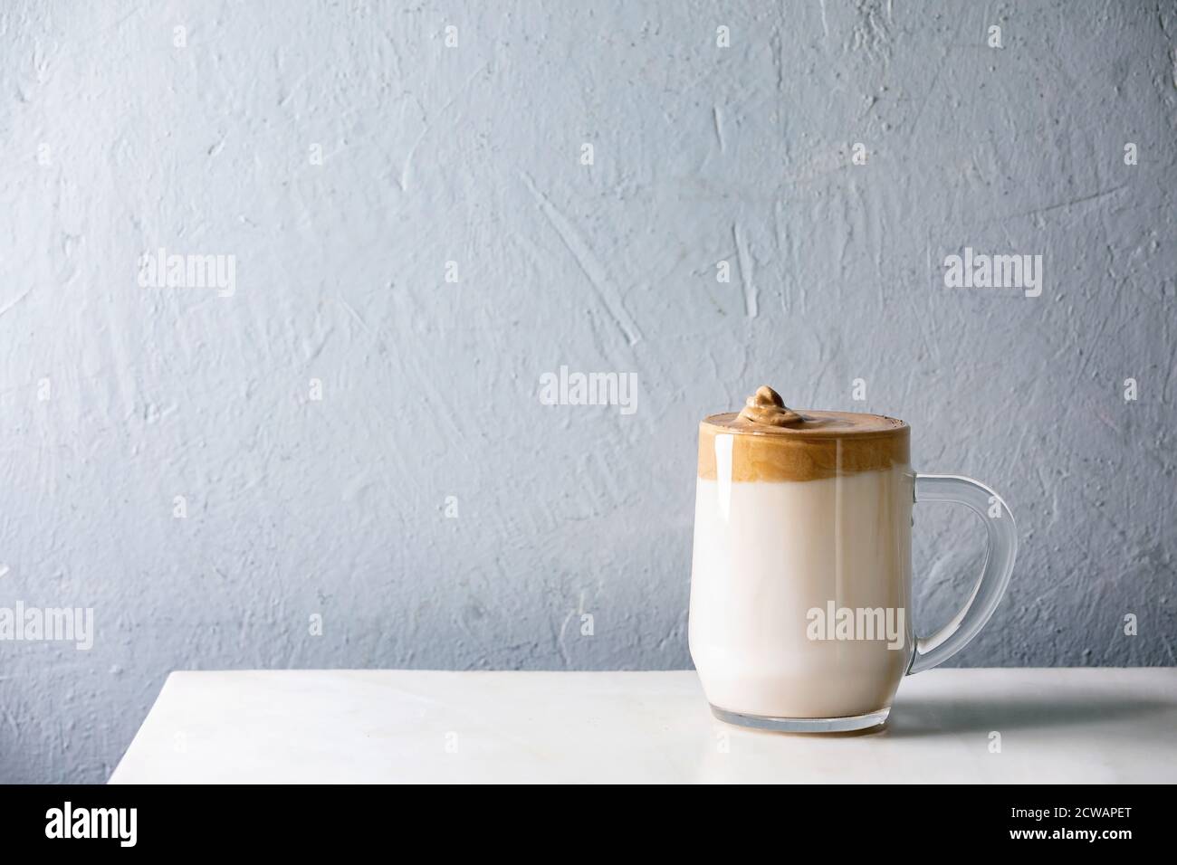 Dalgona Frothy caffè tendenza bevanda coreana latte latte latte con schiuma di caffè in tazza di vetro su tavolo di marmo bianco. Spazio di copia Foto Stock
